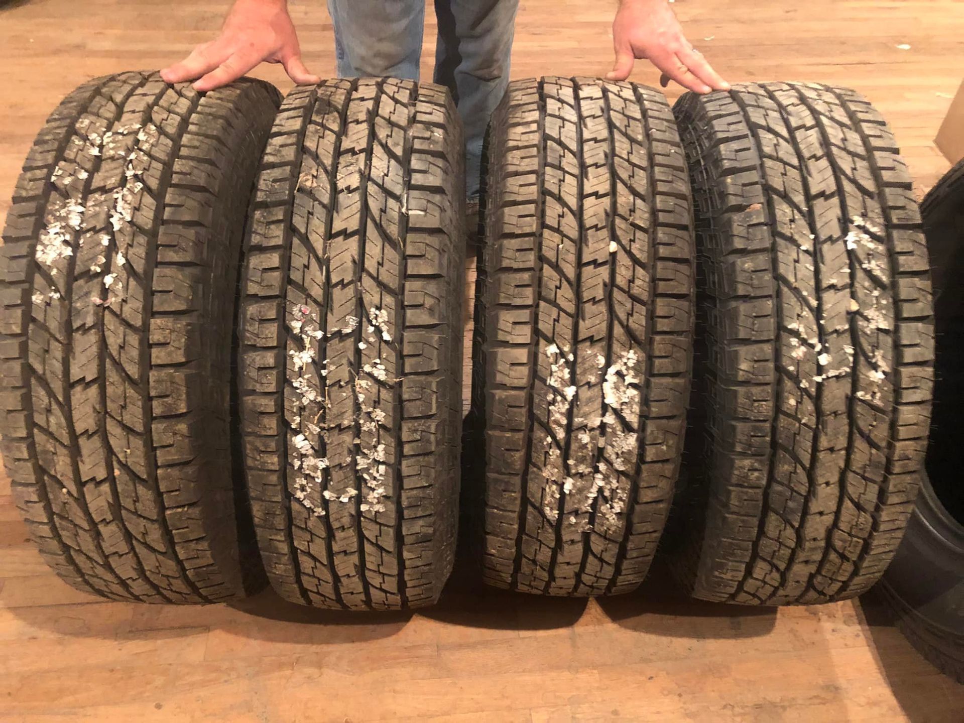 Four rugged tires lined up side by side, with hands visible behind them.