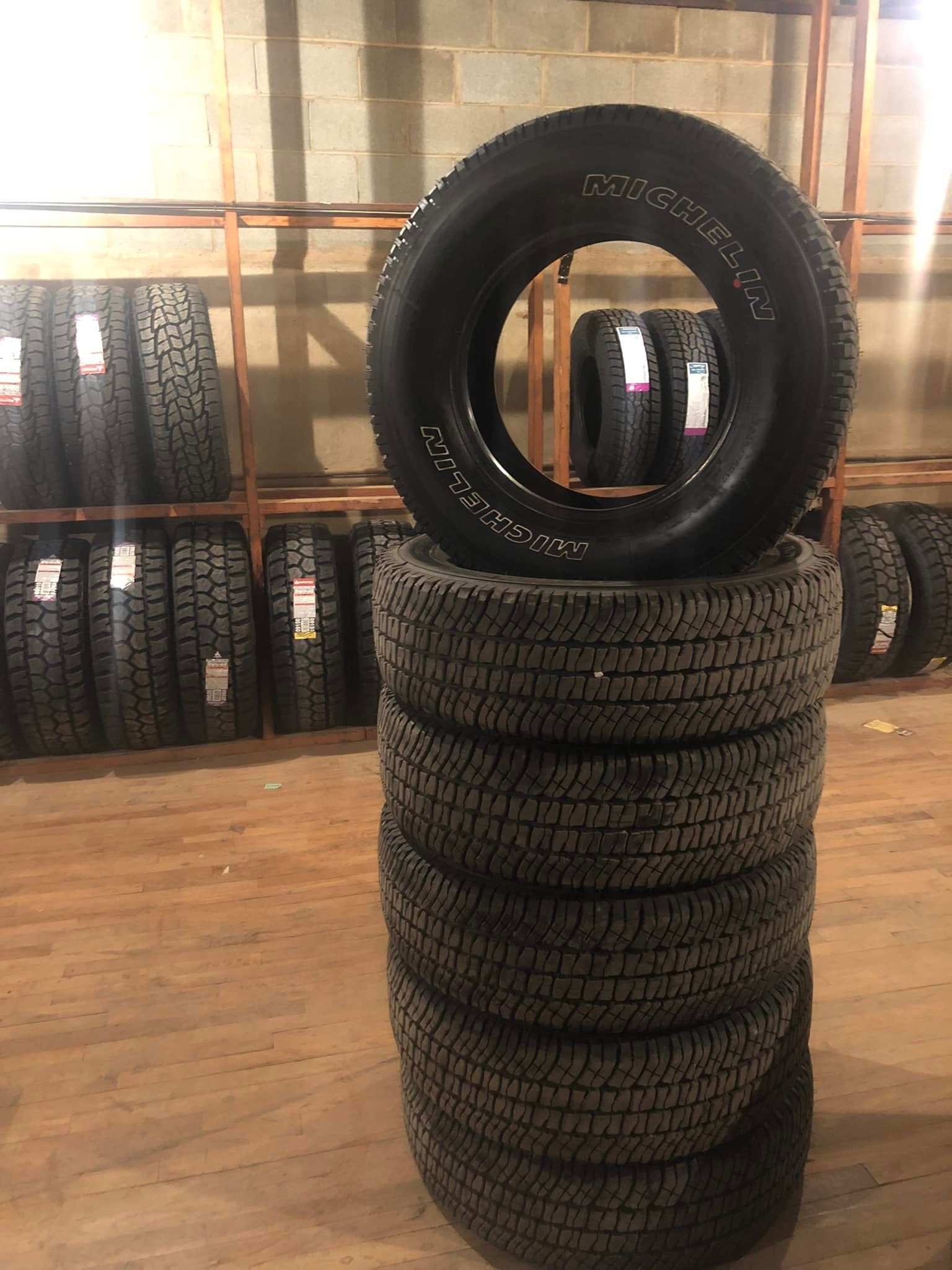 Stack of tires in a warehouse, with a single tire standing on top against a wooden wall.