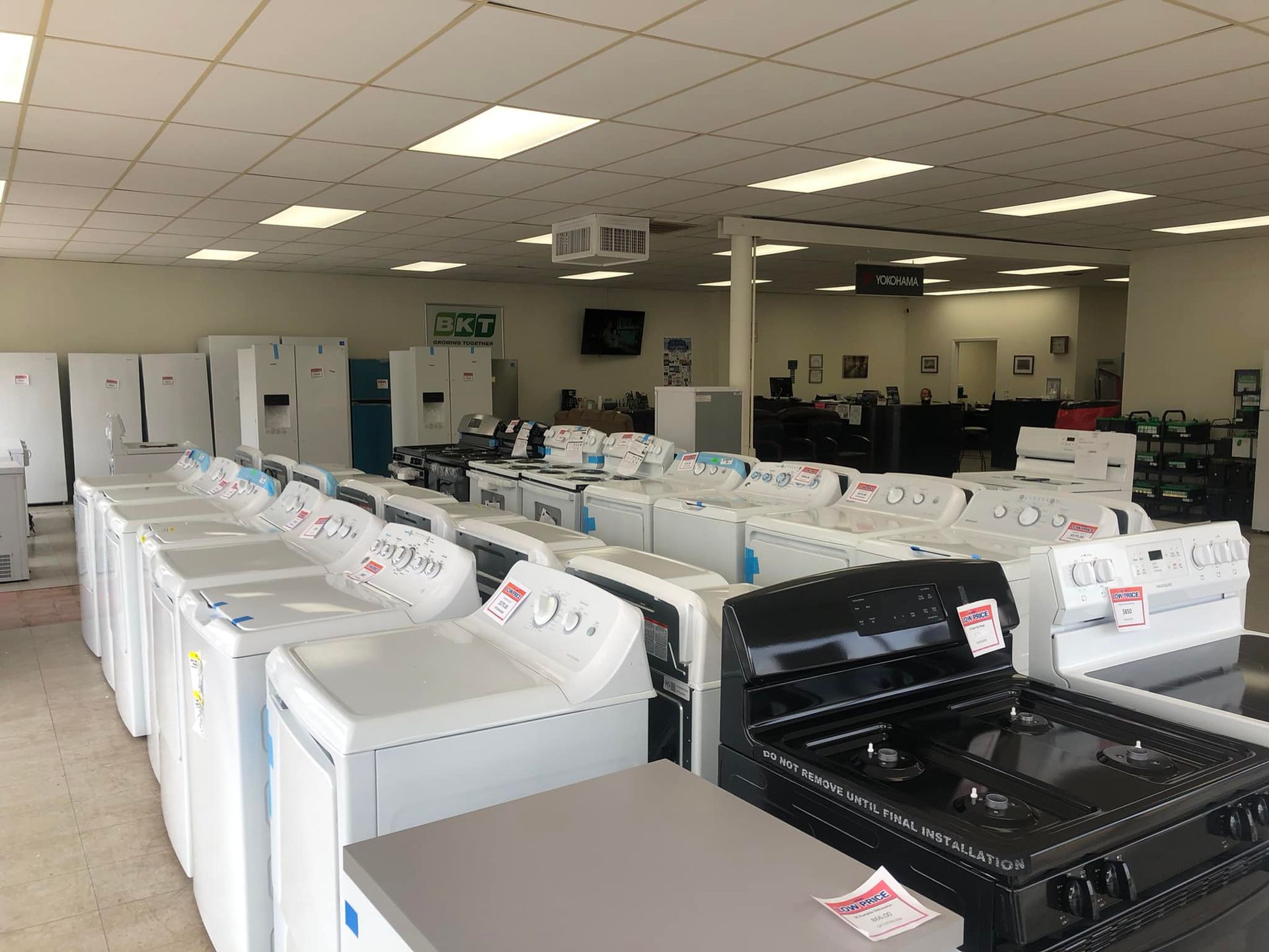 Appliance showroom with rows of washers and dryers under fluorescent ceiling lights