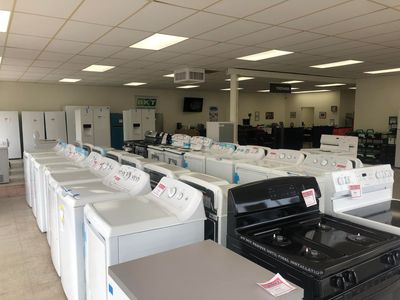 Appliance store showroom with rows of washing machines, dryers, and stoves under fluorescent lights