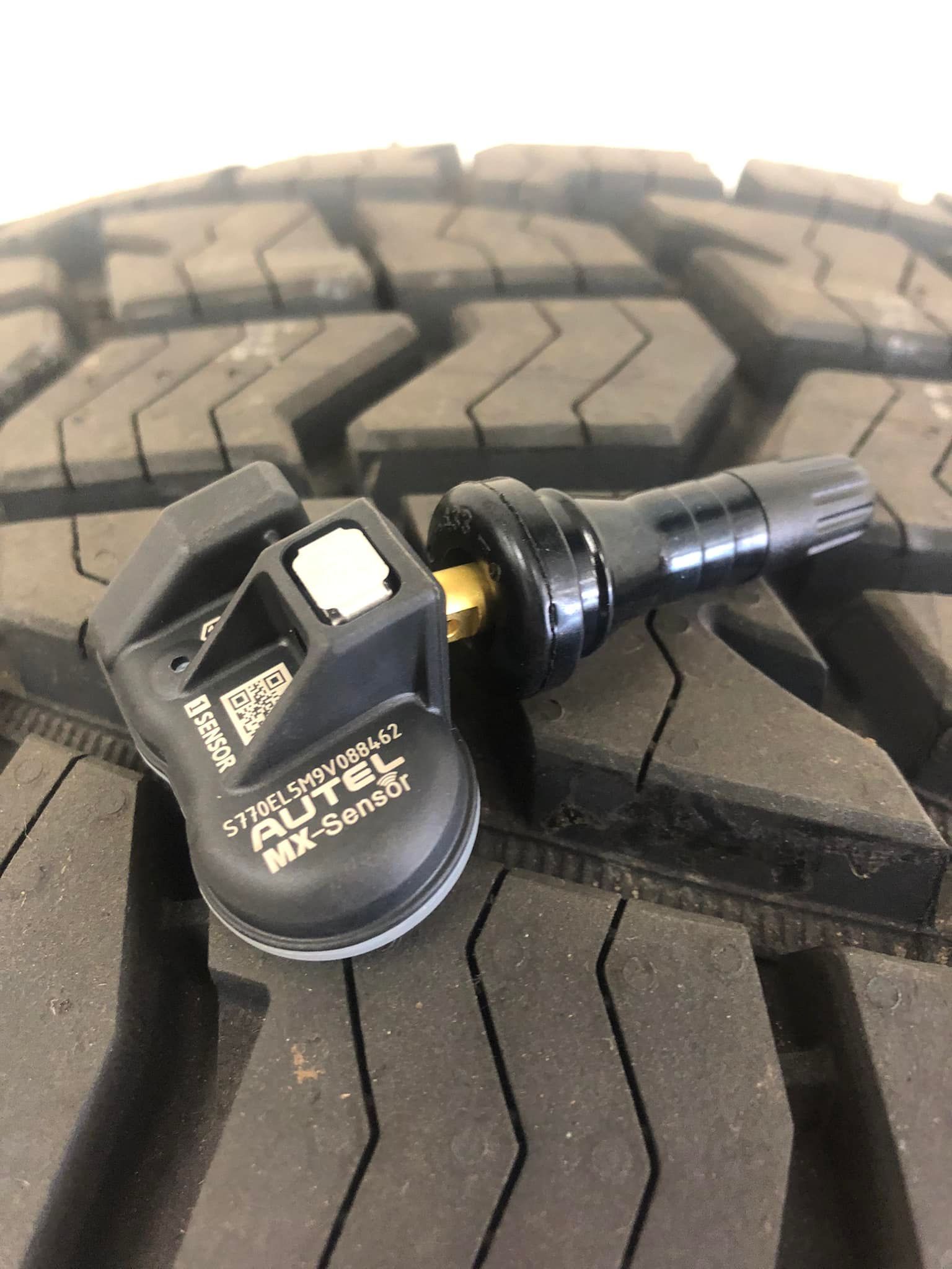 Tire pressure monitoring valve stem cap on a tire tread, black with white markings.