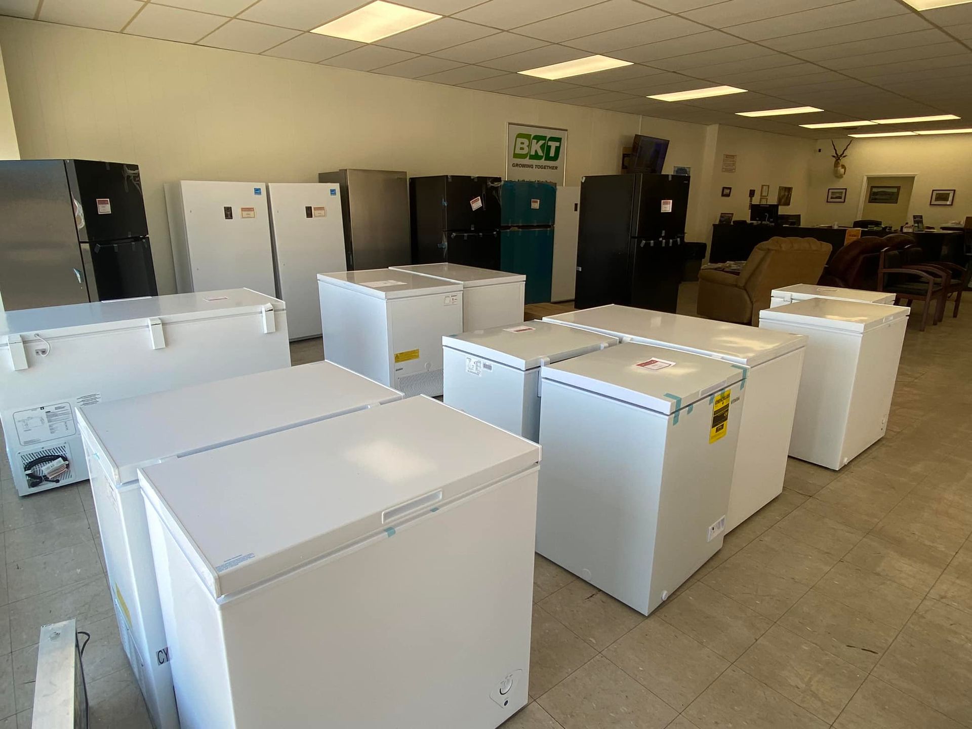 Appliance showroom with rows of white refrigerators and freezers on a tiled floor