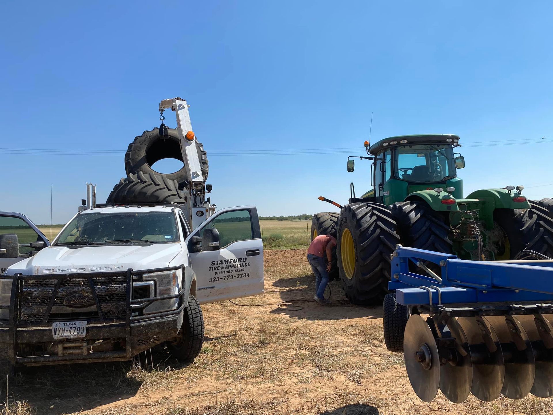 White pickup and green tractor with farm equipment on a dry field under a clear blue sky