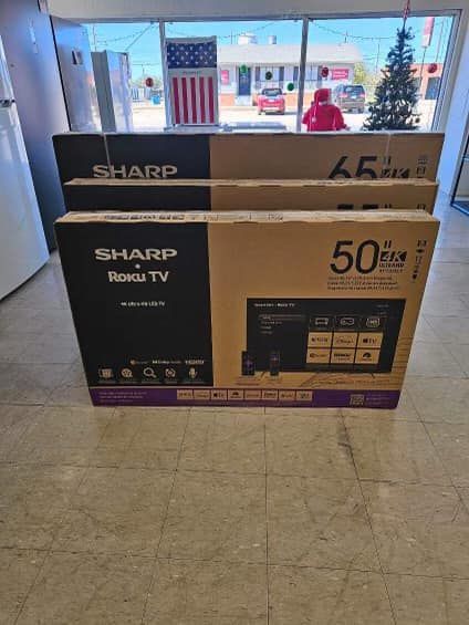 Two SHARP Roku TV boxes in a store aisle, one marked 50-inch and one 65-inch.