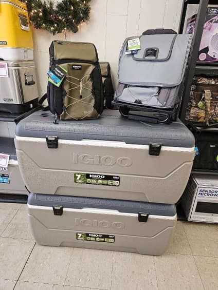 Two beige Igloo coolers stacked on a tiled floor with camping chairs behind them.