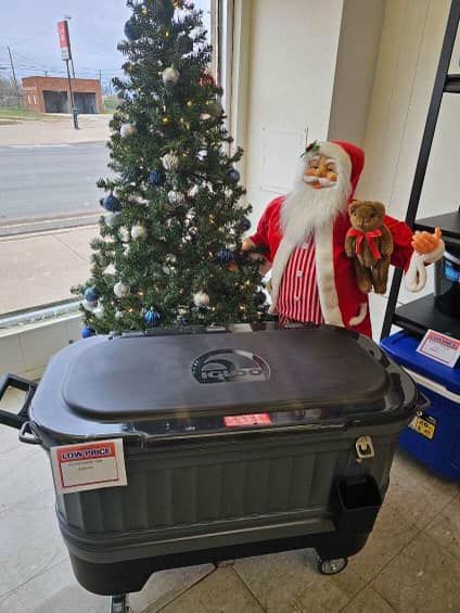 Christmas tree and Santa decoration beside a black rolling storage bin in a store window.