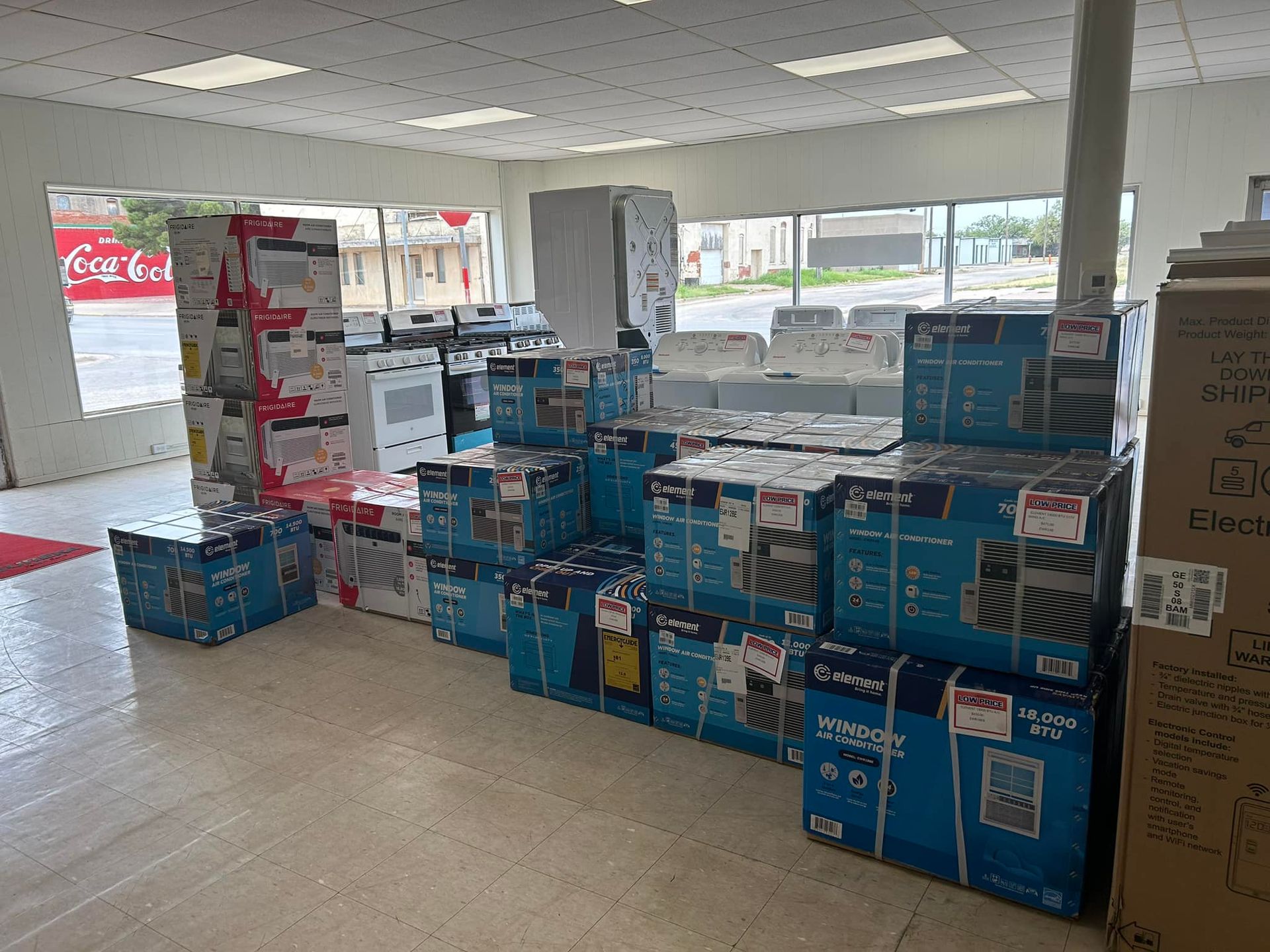 Stacked blue appliance boxes in a store aisle near a windowed showroom.