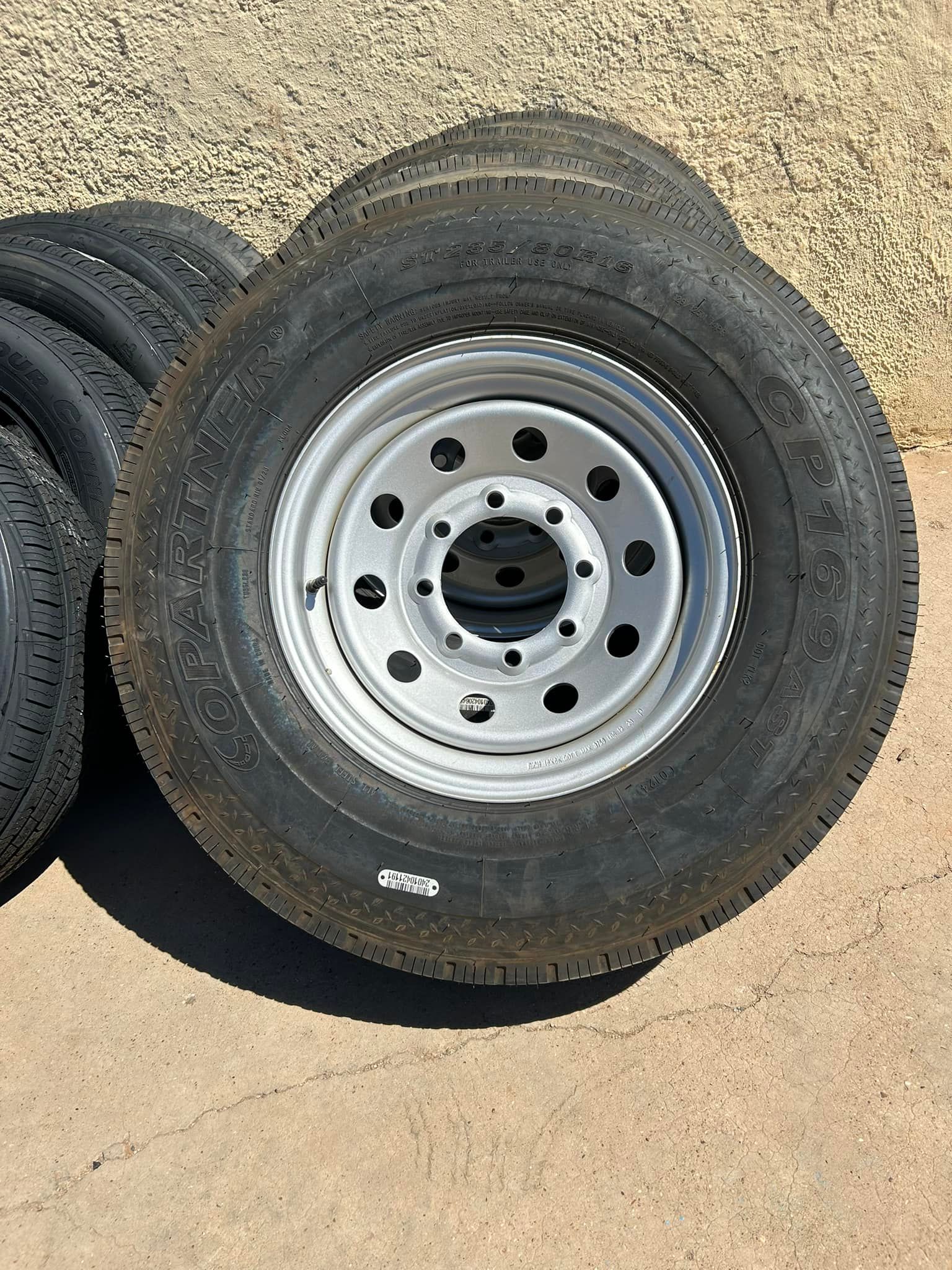 Stacked black vehicle tires with silver steel rims on a concrete surface.