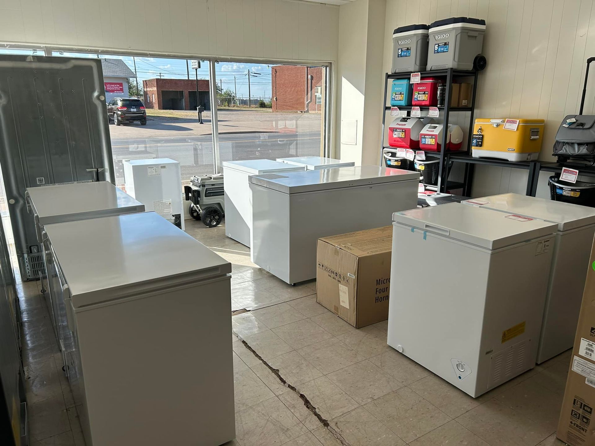 Indoor warehouse with large white appliances and boxes near an open garage door.