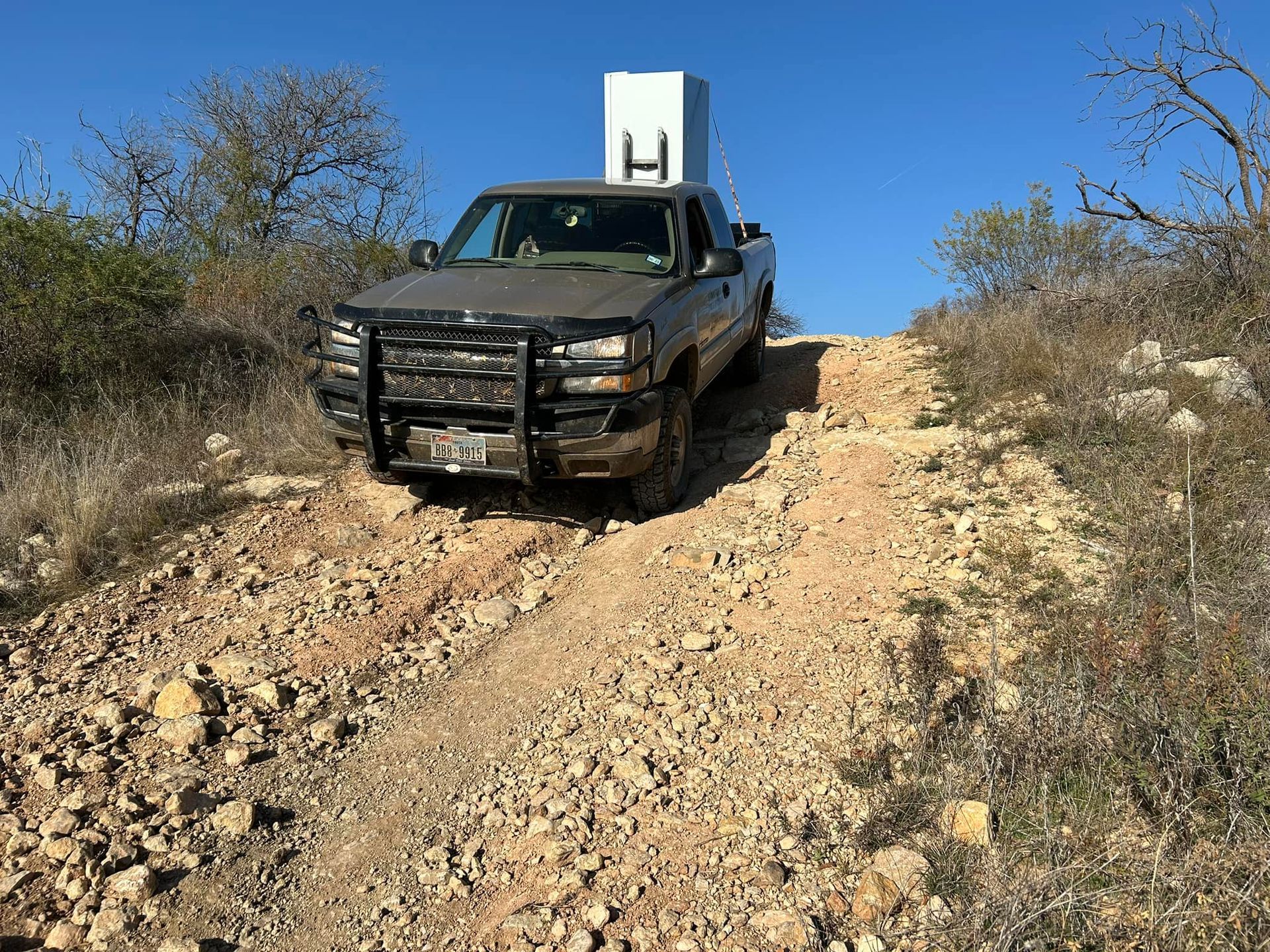 Black pickup truck on a rocky dirt hill road under a clear blue sky