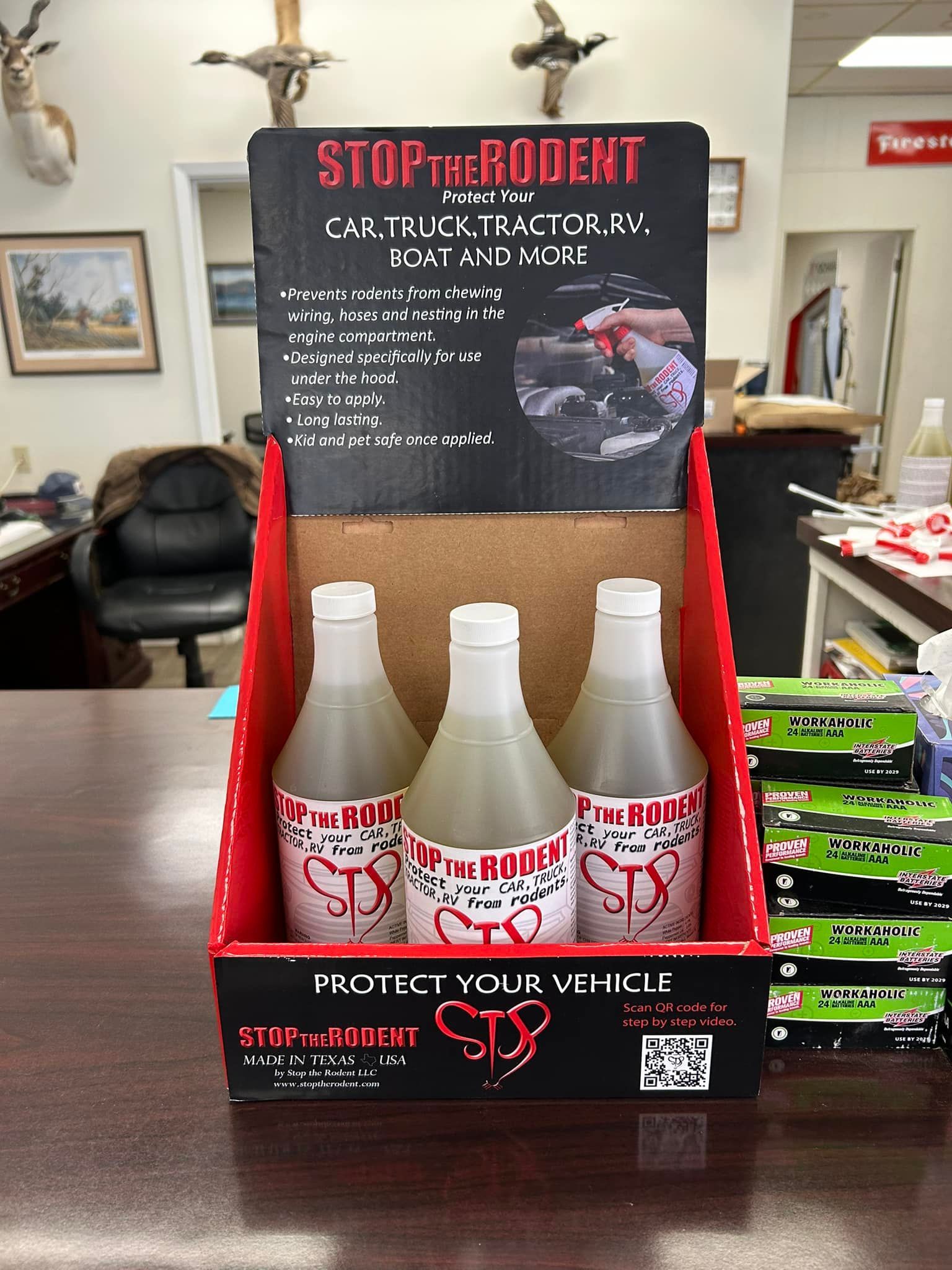 Store display of white bottles in a red cardboard counter display on a desk, with a black promotional sign above.