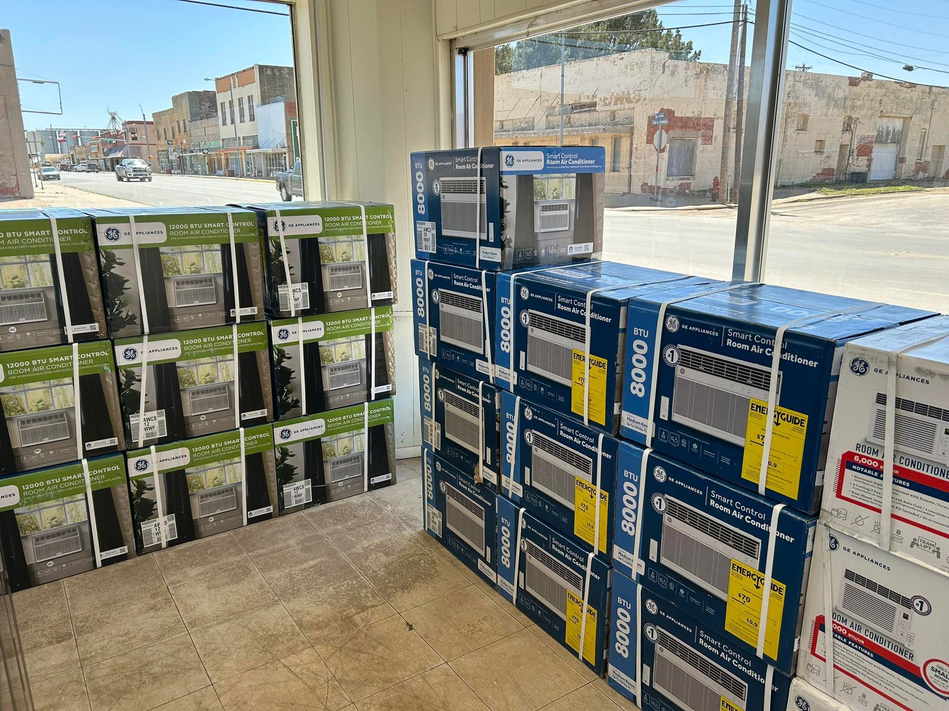 Stacked boxed appliances in a storefront, with black-and-green boxes on the left and blue-and-white boxes on the right.