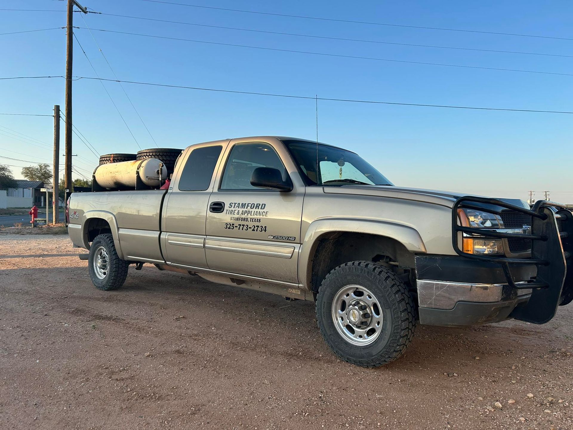 Silver pickup truck parked on dirt road at sunset, with utility tanks in the bed and a front grille guard