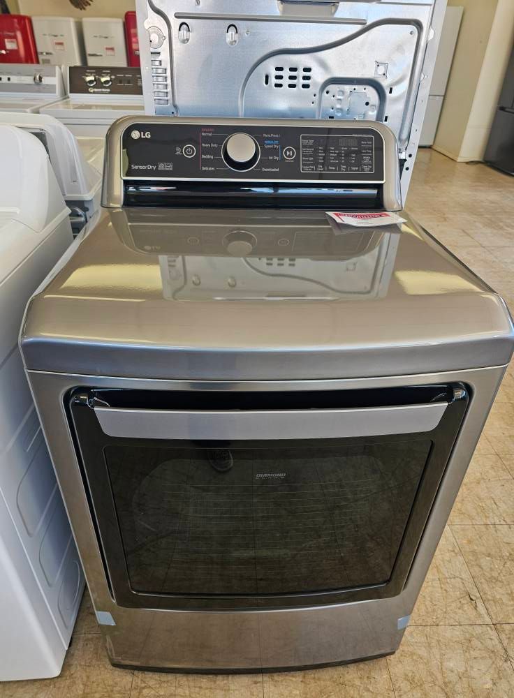 Stainless steel front-load dryer with control panel, shown in a laundry room or appliance store.
