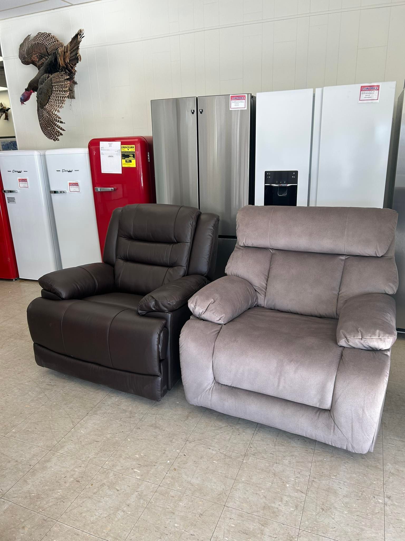 Two recliner chairs, one dark brown and one light gray, in a furniture showroom
