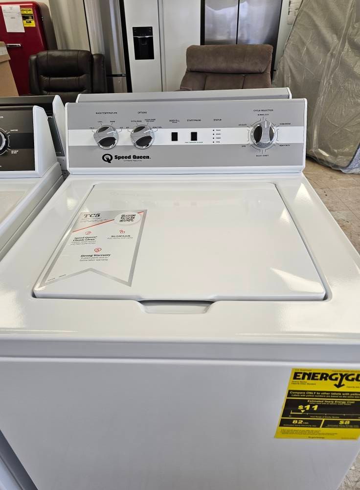 White top-load washer with control panel, in a laundromat-like room, with an energy label on the front.