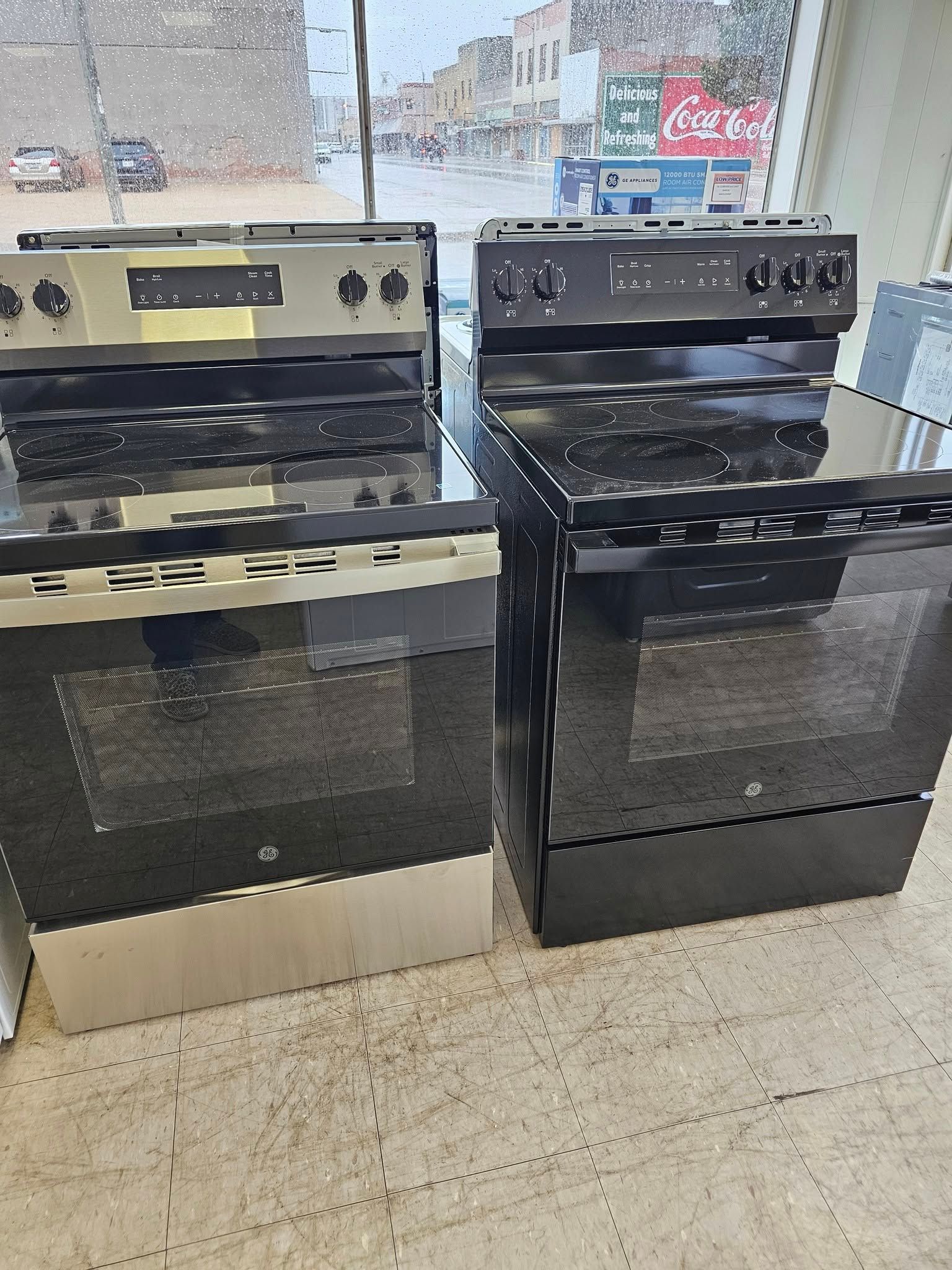 Two black electric ranges with glass oven doors displayed in a store aisle.