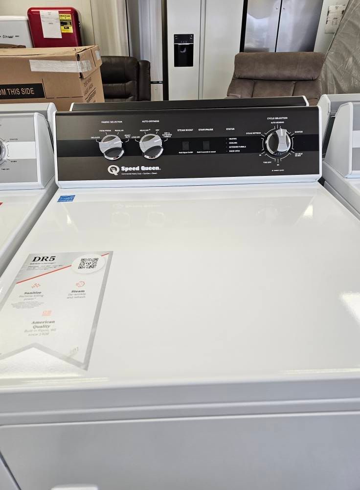 White top-load washing machine with black control panel in a laundry room showroom.