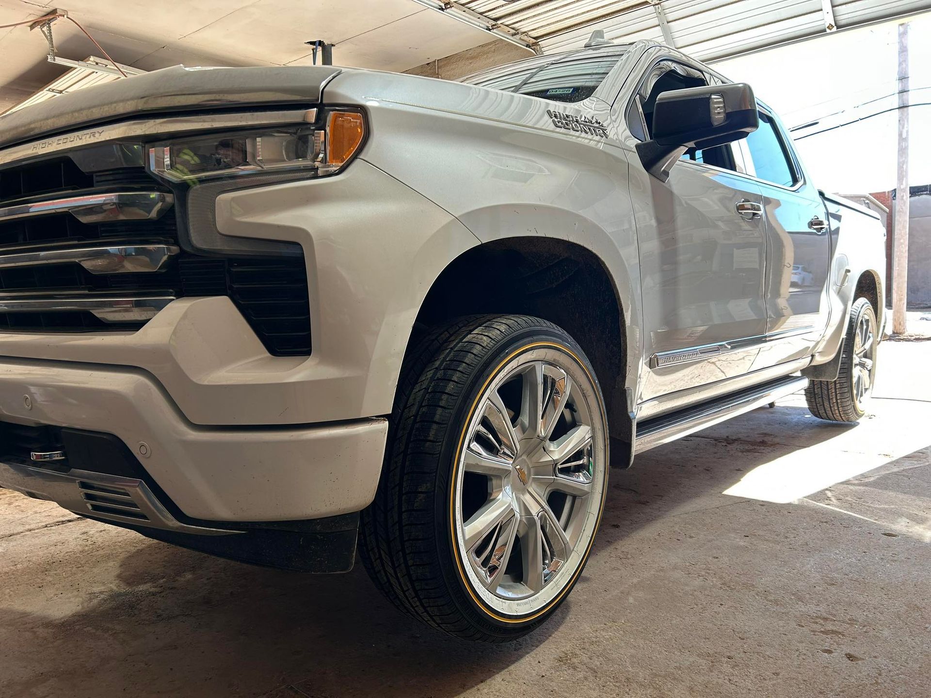 White pickup truck parked inside a garage, shown from the front-left side with chrome wheels.
