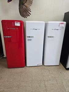 Three retro refrigerators—red, white, and white—lined up indoors against a wall.