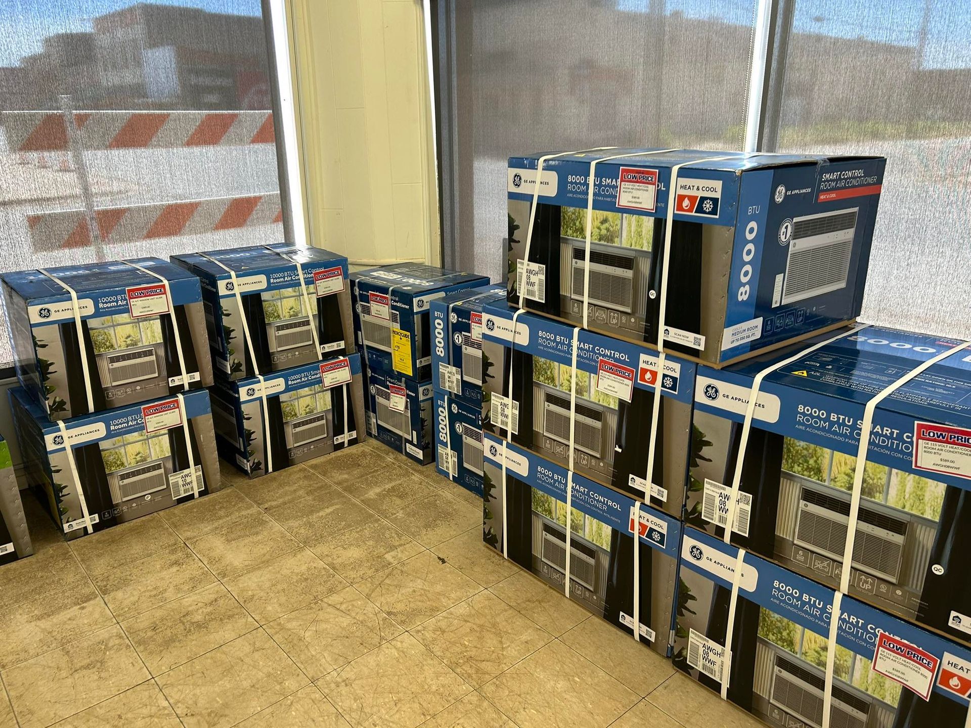 Stacks of boxed appliances piled on a store floor beside a window.