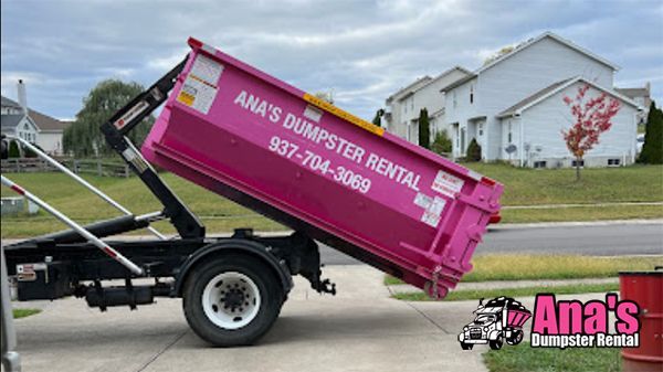Pink dumpster on a black truck, labeled “Ana’s Dumpster Rental,” in a suburban neighborhood