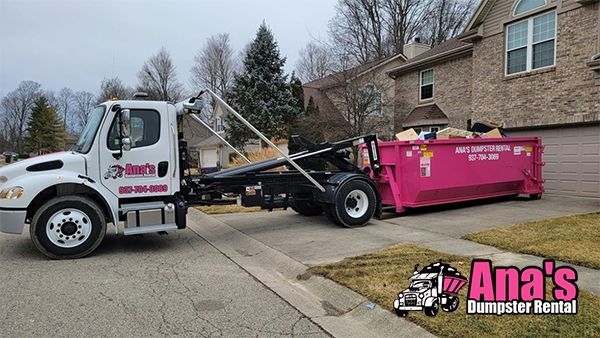 Dumpster truck lifting a bright pink dumpster in a residential driveway