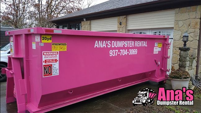 Bright pink Ana’s Dumpster Rental dumpster parked outdoors beside a house.