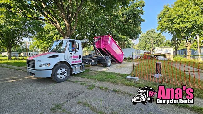 White dump truck raising a bright pink dumpster in a residential yard with a fencing crew logo.