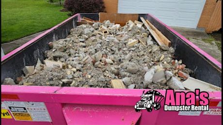 Pink dumpster filled with rubble and debris in a driveway beside a house