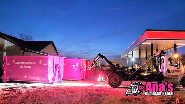 Pink-lit shipping containers and a forklift at dusk outside a building labeled “Ana’s”