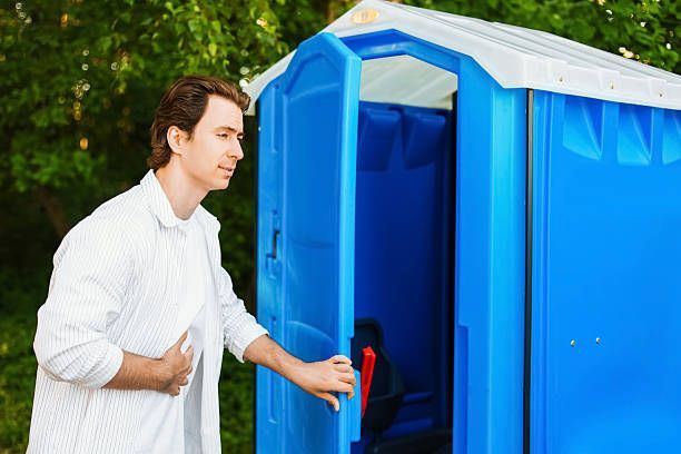 Man opening the door of a blue portable toilet outdoors