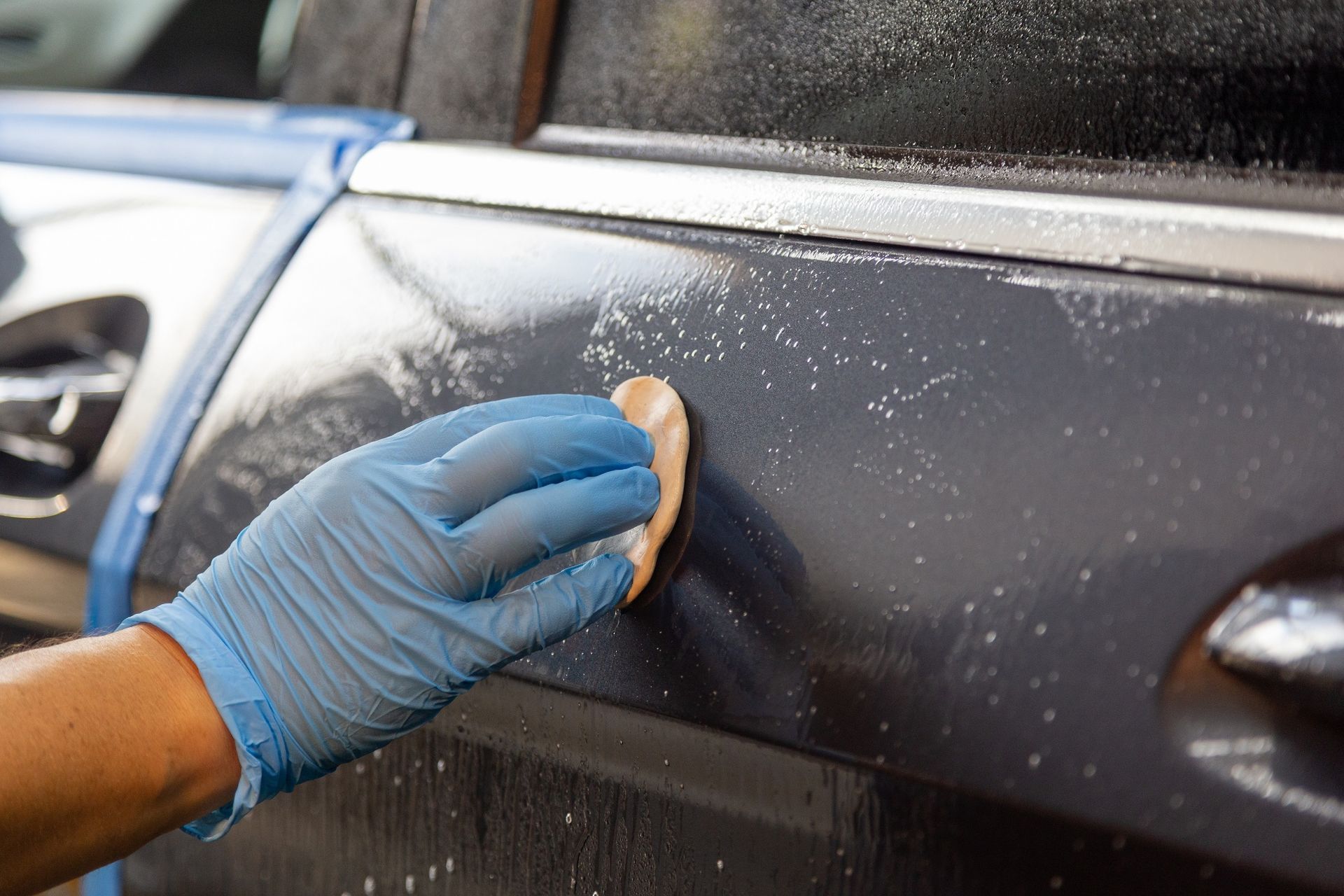 Gloved hand scrubbing dirt off a black car door with a sponge