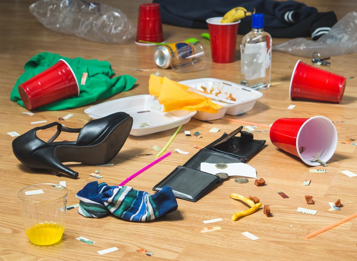 Messy wooden table with spilled snacks, red cups, a black shoe, and scattered trash and wrappers