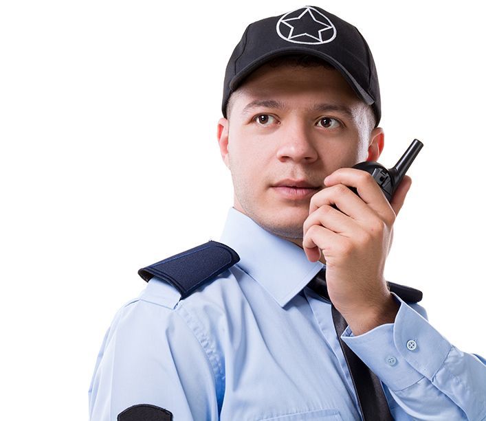 Security guard in light blue uniform speaking into a handheld radio, wearing a black cap.