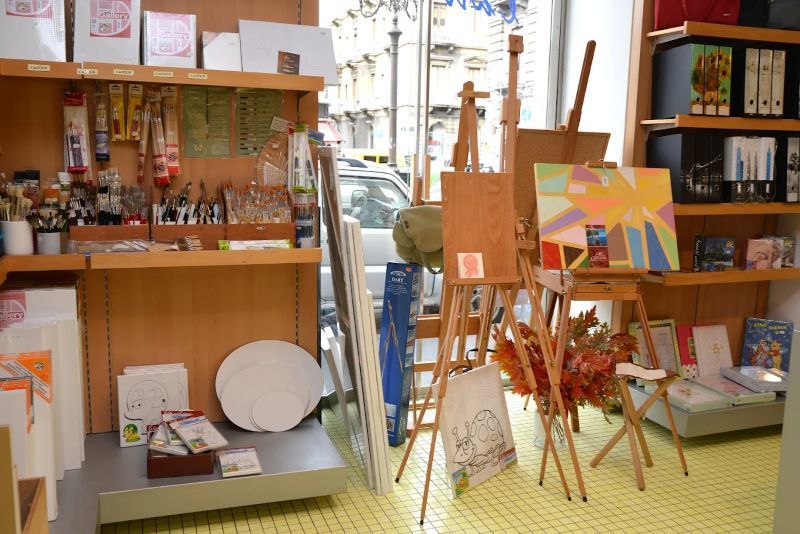 Interno di una galleria d'arte con scaffali, cavalletti e dipinti colorati in esposizione.