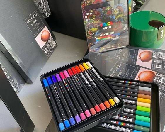 Pennarelli colorati e scatole di materiali artistici disposti su una scrivania, con del nastro adesivo verde sullo sfondo.
