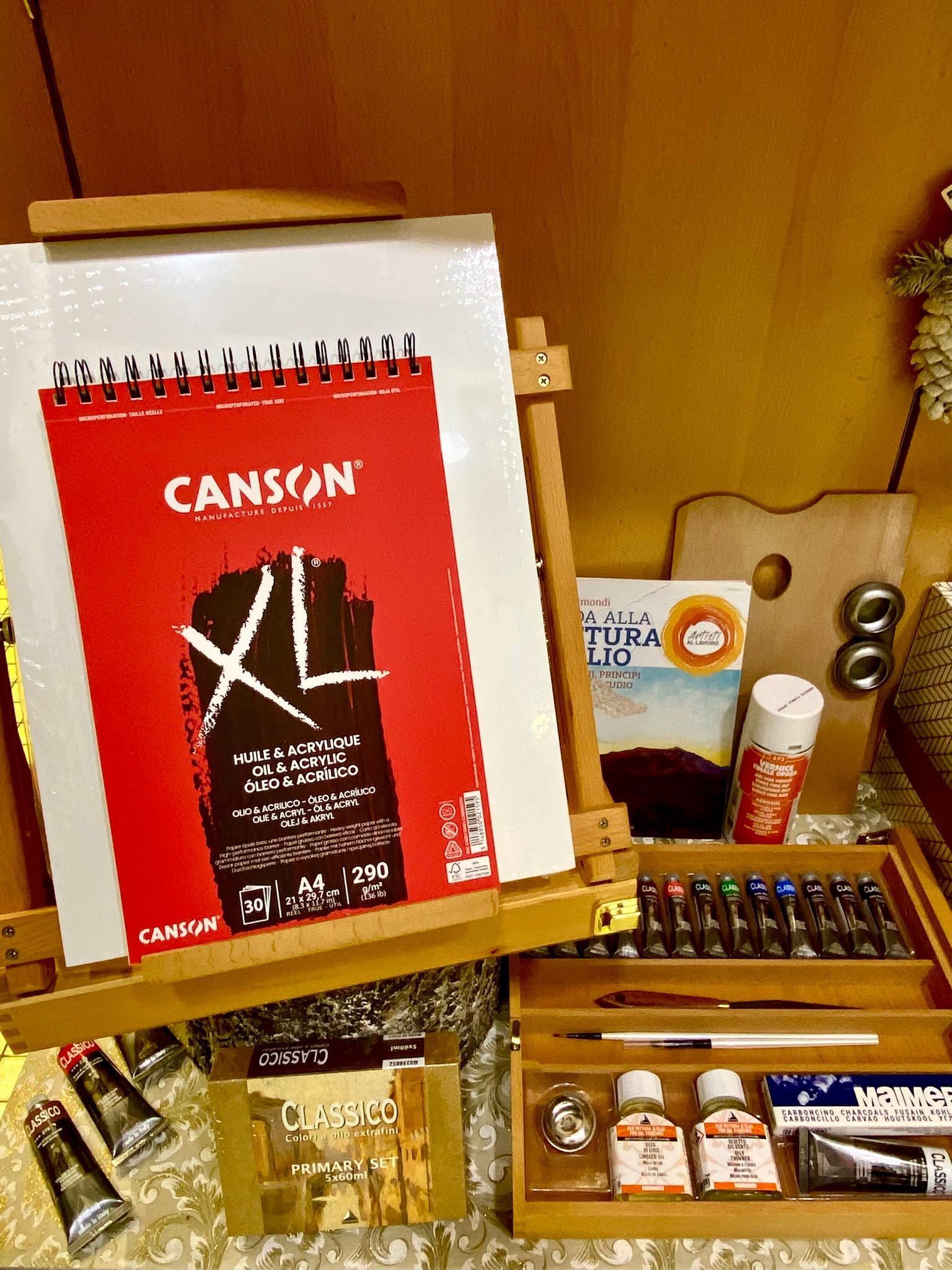 Mensola da scrivania con un blocco da disegno Canson XL rosso, penne e piccoli materiali artistici disposti in scomparti.