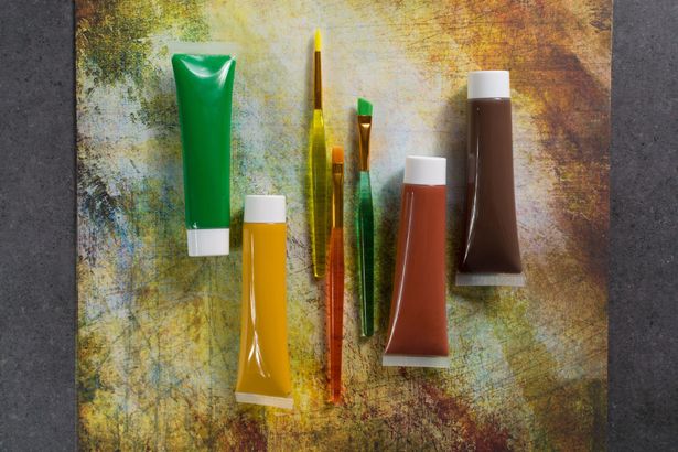 Cinque tubetti di colore e due pennelli su uno sfondo multicolore e dalla texture particolare.