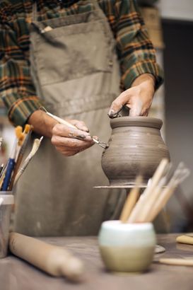 Un vasaio modella un vaso di argilla al tornio, con attrezzi e pennelli, in un laboratorio.