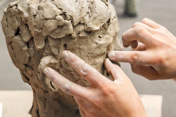 Mani che modellano una scultura di argilla su un tavolo da lavoro, primo piano.