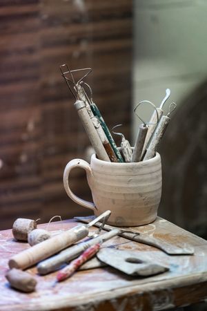 Tazza di terracotta contenente pennelli e strumenti da disegno su un tavolo di legno con schizzi e materiali artistici