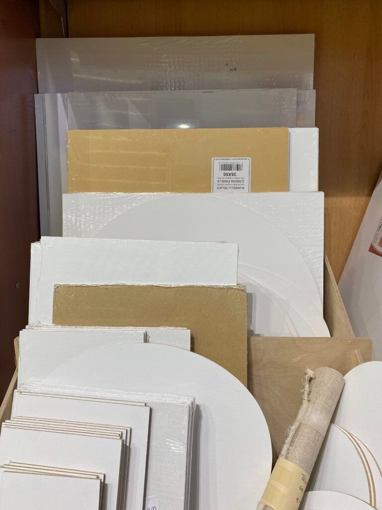 Una pila di carte e cartoncini di vario tipo, dai toni neutri, appoggiata verticalmente a una parete.