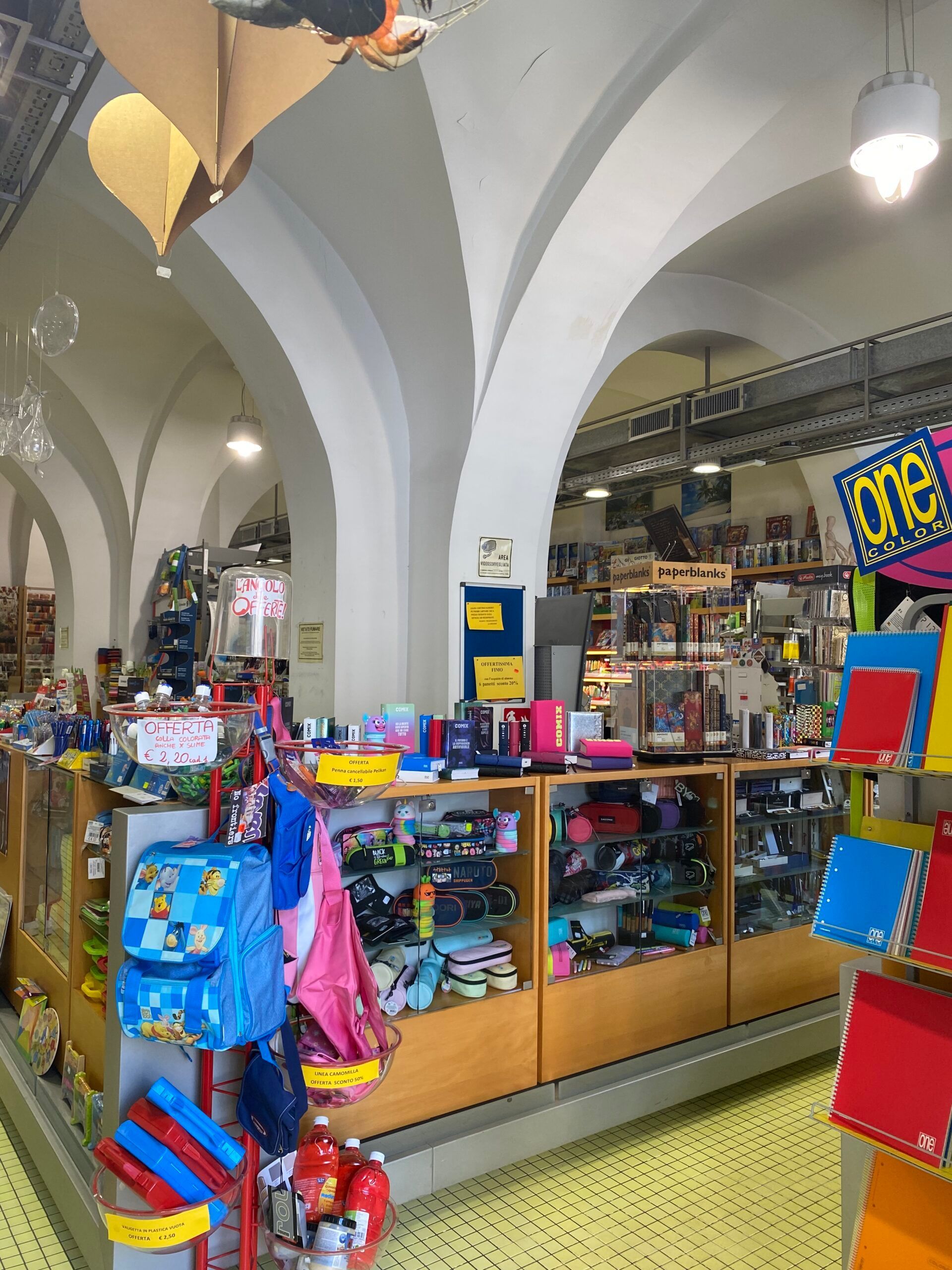 Bancarella al coperto con giocattoli colorati, borse e souvenir sotto soffitti ad arco bianchi.