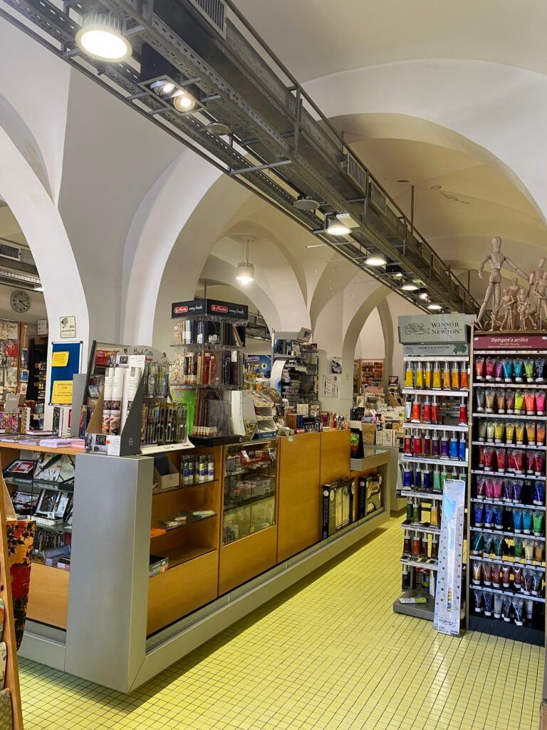 Bancarella in un mercato coperto con soffitto a volta, scaffali pieni di oggetti colorati e pavimento piastrellato di giallo.