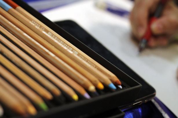 Matite colorate in un astuccio nero con un disegno a mano sullo sfondo sfocato.
