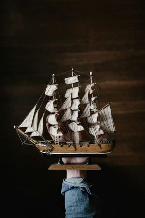 Modellino di veliero con diverse vele bianche su un supporto, su sfondo scuro.