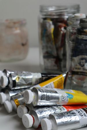 Tubetti di colore assortiti sparsi su un tavolo, con barattoli di vernice sullo sfondo.