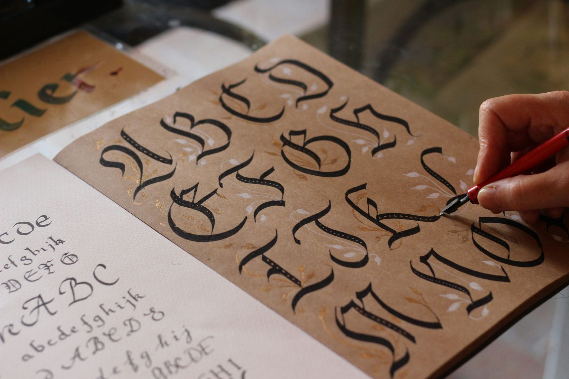 Mano che si esercita nella calligrafia su un foglio di lettere nere stilizzate con una penna rossa