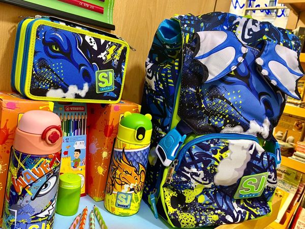 Set di zaini scolastici colorati con portapranzo e borracce abbinati, su un tavolo dai colori vivaci.